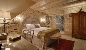 A bedroom with a stone wall, a bed, a wooden cabinet, and a red rug. - Kamares Boutique Hotel & Spa Ioannina (Ioannina)