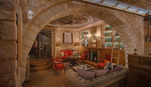 A room with a stone archway, a red sofa, a round coffee table, and a bookshelf with various items. - Kamares Boutique Hotel & Spa Ioannina (Ioannina)
