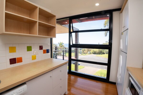 A kitchen with white cabinets, a wooden countertop, and a large window with a view of a road and greenery.