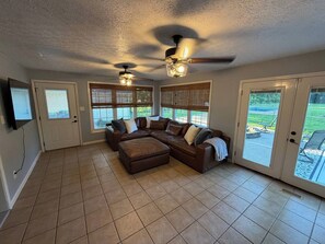 A spacious living room with a sectional sofa, ceiling fans, and large windows.