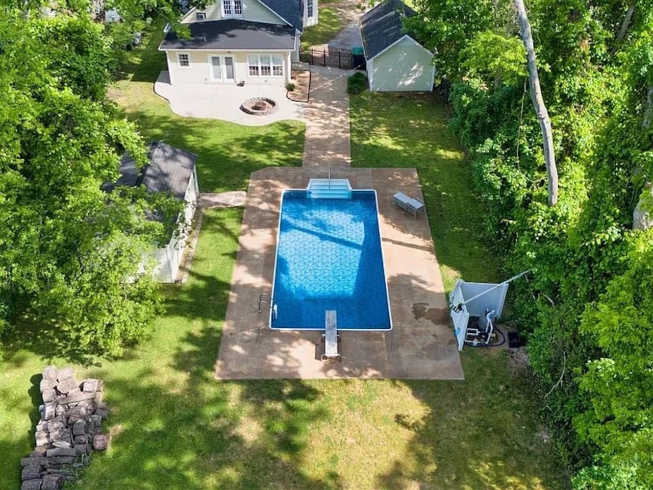 Patio trasero residencial con piscina, muro de piedra y una casa.