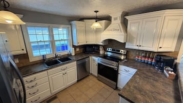Una cocina con gabinetes blancos, estufa de acero inoxidable, microondas y cafetera.
