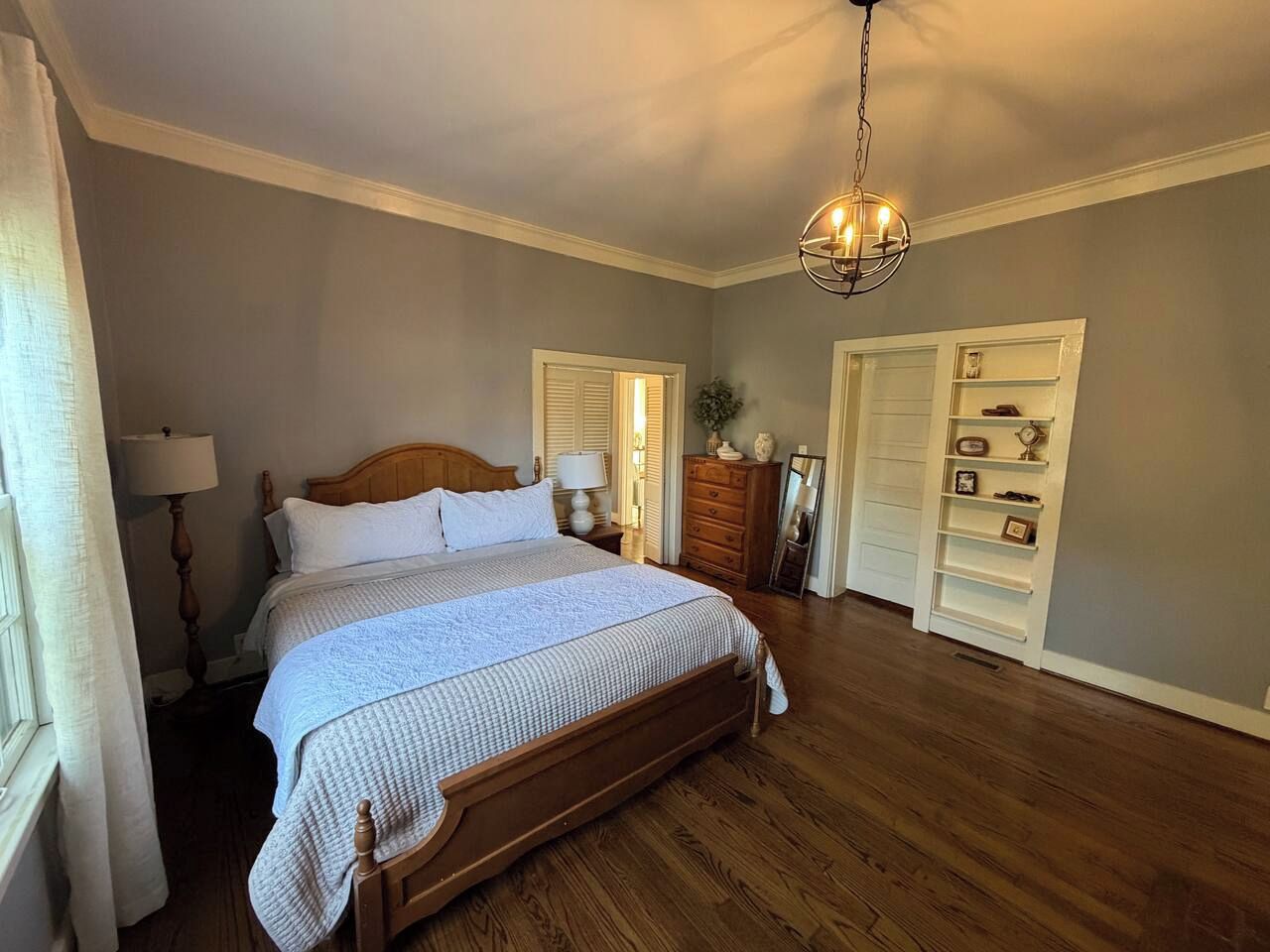Un dormitorio con una cama grande, suelo de madera, un candelabro, un aparador y un armario.