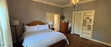 Ein Schlafzimmer mit einem großen Bett, Holzböden, einer Kandelaberleuchte, einem Schminktisch und einem Kleiderschrank.