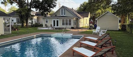 A swimming pool with lounge chairs and a house in the background.