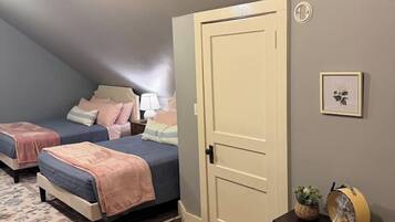 Ein Schlafzimmer mit zwei Betten, einer Tür, einem kleinen Tisch mit Ventilator und einem gerahmten Bild an der Wand.