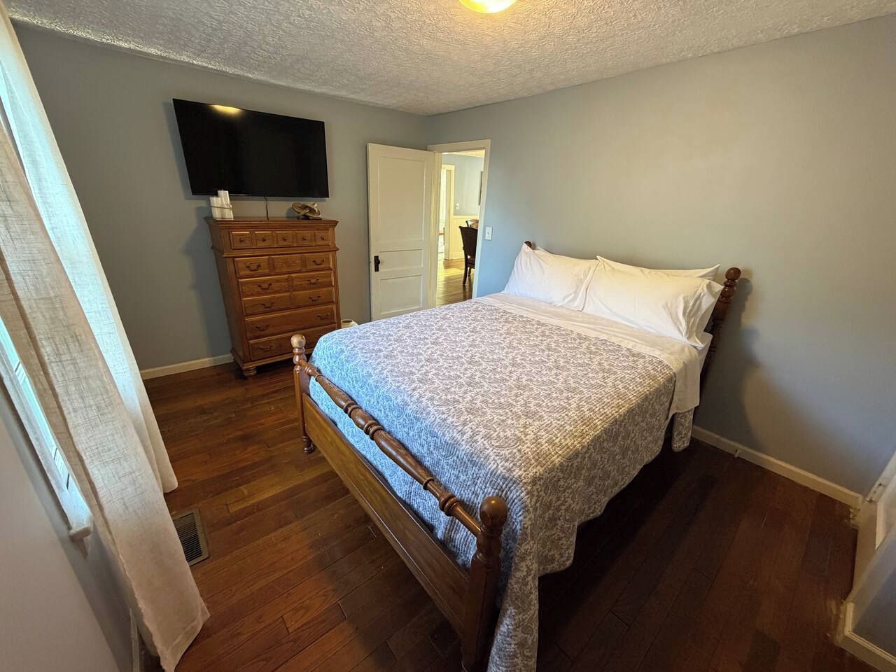 A bedroom with a wooden bed, a dresser, and a television on the wall.