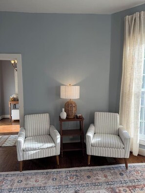 A room with two striped armchairs, a side table with a lamp, and a patterned rug.