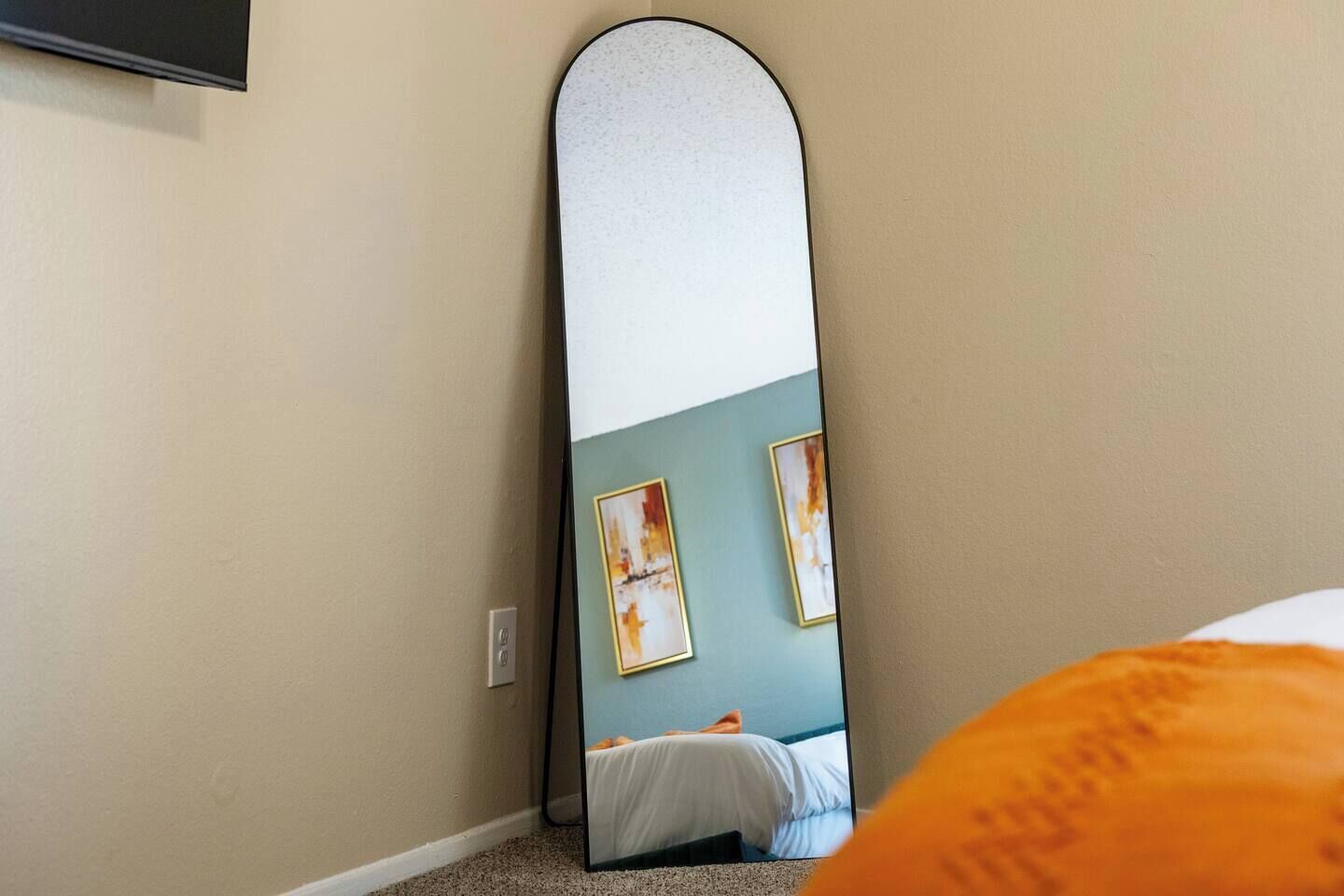 A room with a bed, a wall-mounted TV, and a large mirror reflecting the room.