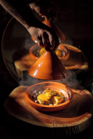A traditional Moroccan tagine cooking method with a hand lifting the lid. - Mia Agafay Resort (Agafay)