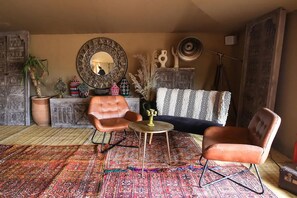 A living room with a patterned rug, two leather armchairs, a round coffee table, a sofa, decorative items, and a large mirror. - Mia Agafay Resort (Agafay)