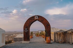 An archway with the logo of MIA AGAFAY RESORT, leading to a desert landscape with tents and cacti. - Mia Agafay Resort (Agafay)