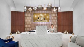 Una recepción con encimera de mármol, un cartel que dice 'Jala Spa & Wellness' y una recepcionista.