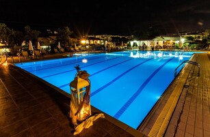 Una piscina con agua azul cristalina, rodeada de tumbonas y sombrillas, y una zona de terraza de madera.