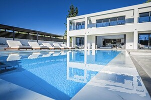 Um edifício moderno de dois andares com piscina, espreguiçadeiras e um terraço coberto.