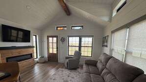 A living room with a fireplace, a television, a sofa, and a window with a view of the outdoors.