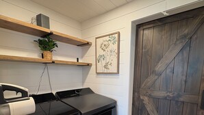 A laundry area with a washing machine, dryer, wooden shelves, a potted plant, and a large wooden door.