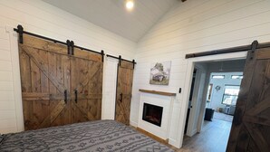 A bedroom with a large bed, wooden sliding doors, a fireplace, and a hallway leading to another room.