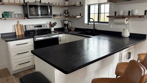 A modern kitchen with a black countertop, stainless steel appliances, white cabinetry, and wooden shelves.
