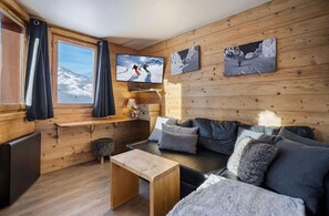Ein gemütliches Blockhaus-Interieur mit Holzwand, einer Couch, einem Fernseher und einem Fenster mit Vorhängen.