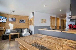 A modern living area with a wooden sofa, a wooden dining table, and a kitchen with a red coffee machine. - sumptueux apartment. 6 people 35m², south-facing, renovated in 2024! (VAL THORENS)