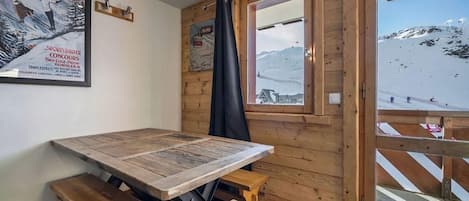 A wooden interior with a table and benches, a window with a view of a snowy mountain, and a poster on the wall.