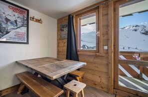 Ein Holzinnenraum mit einem Tisch und Bänken, ein Fenster mit Blick auf einen verschneiten Berg und ein Poster an der Wand.