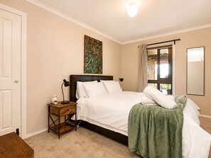 A bedroom with a bed, bedside table, lamp, artwork, window with curtains, and a mirror. - Brindabella Country Escape | Relax, Unwind & Explore (Uriarra)