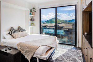 A bedroom with a large bed, a bedside table, a TV stand, a sliding glass door to a balcony, and a view of the outdoors. - Yotelpad Park City (Park City)