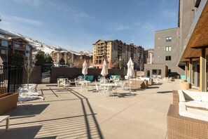 An outdoor patio area with tables and chairs, surrounded by buildings with a view of snow-capped mountains. - Yotelpad Park City (Park City)