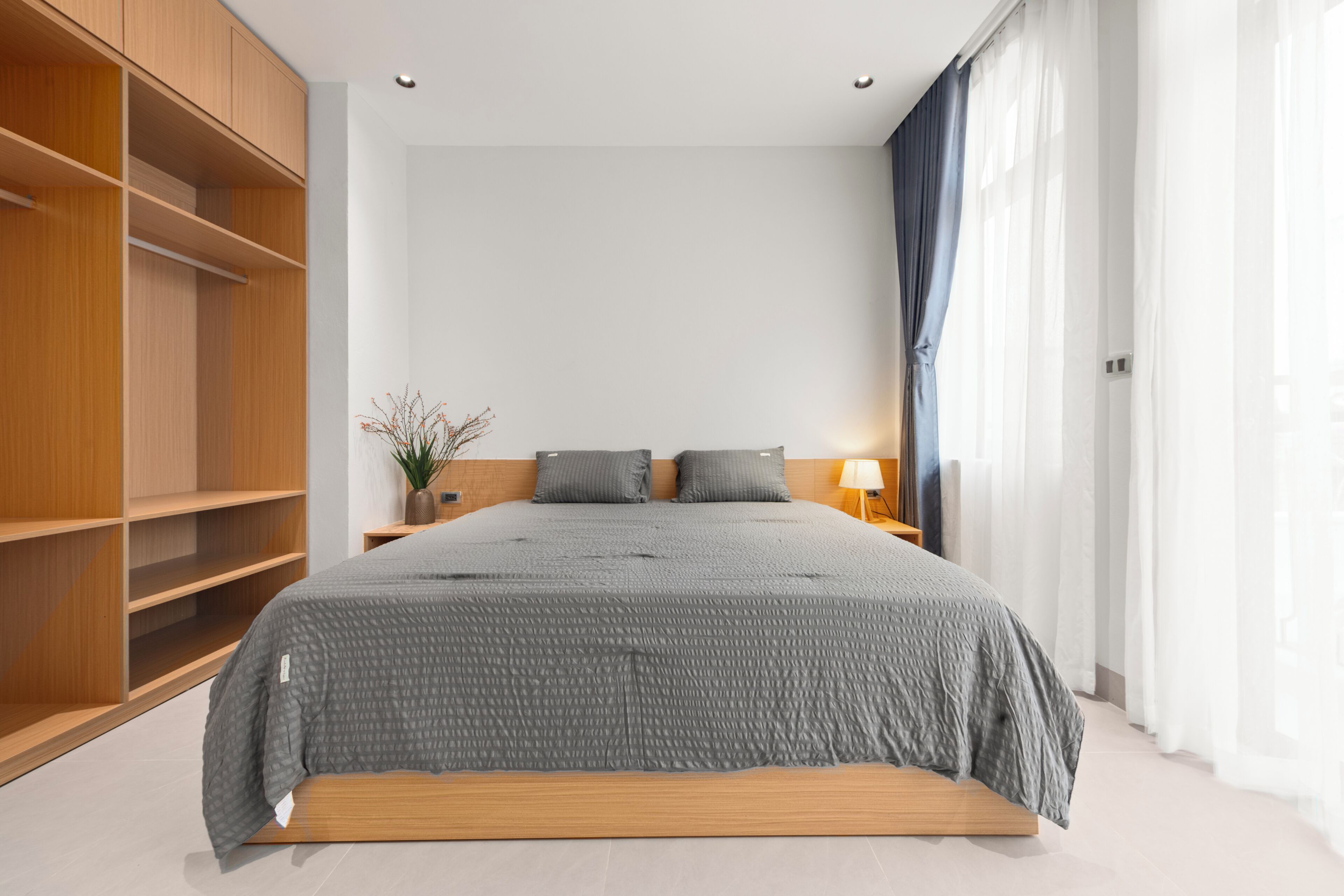 Een moderne slaapkamer met een groot bed, houten planken, een nachtkastje en een raam met gordijnen.