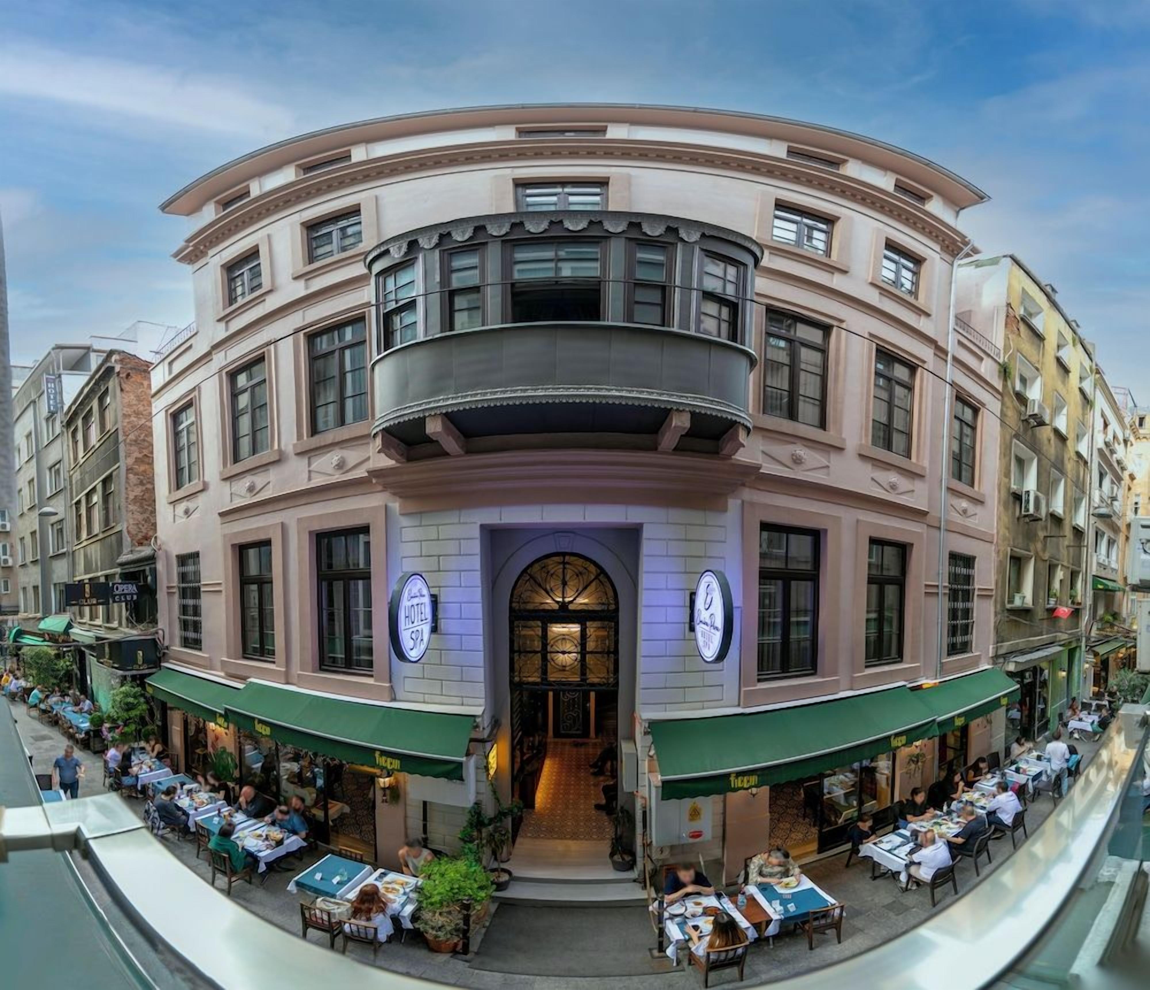 A hotel with a curved facade, outdoor seating, and a clock on the building.