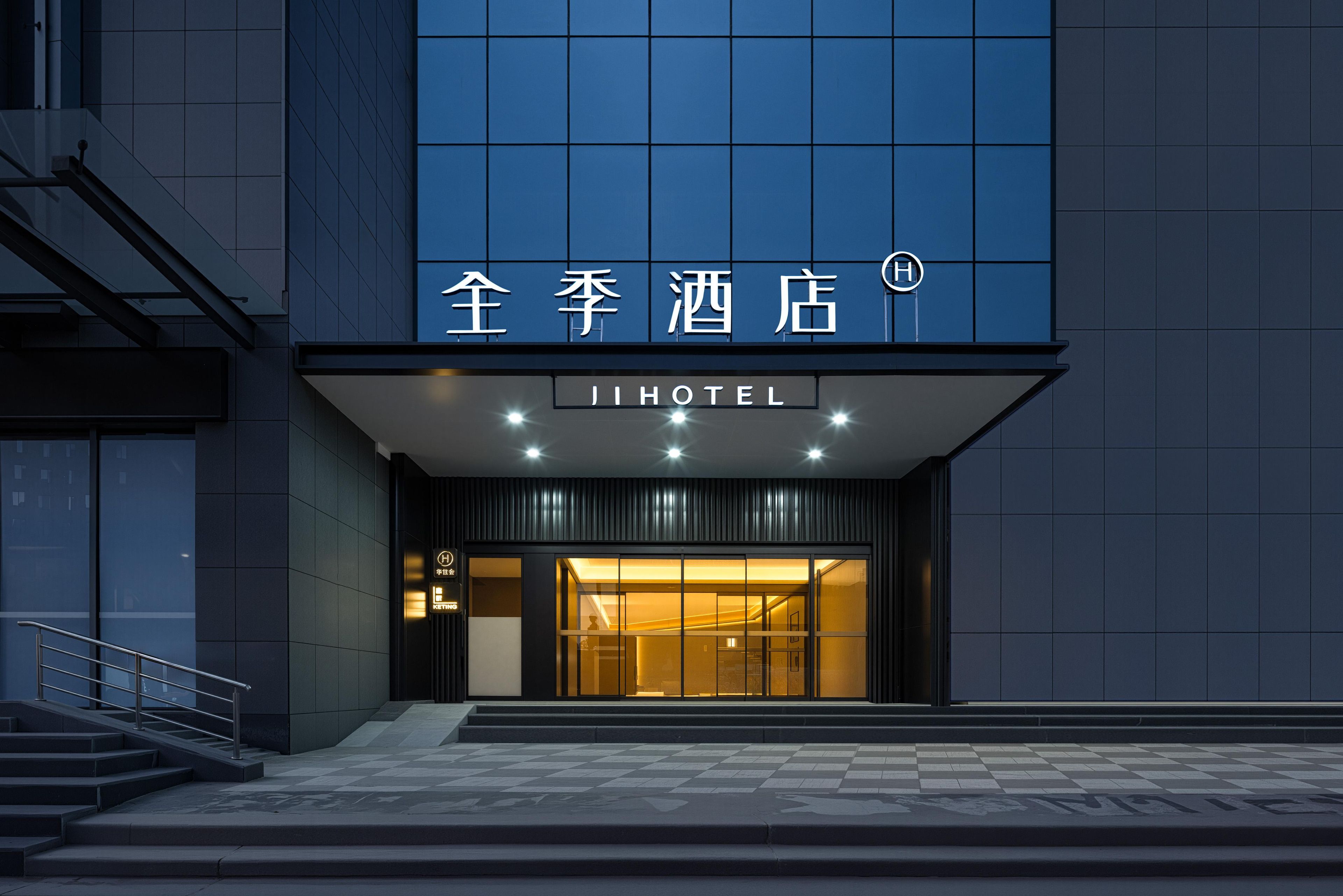 Entrada de hotel com fachada moderna, uma placa indicando o nome 'JI HOTEL' e uma escadaria que leva à entrada.