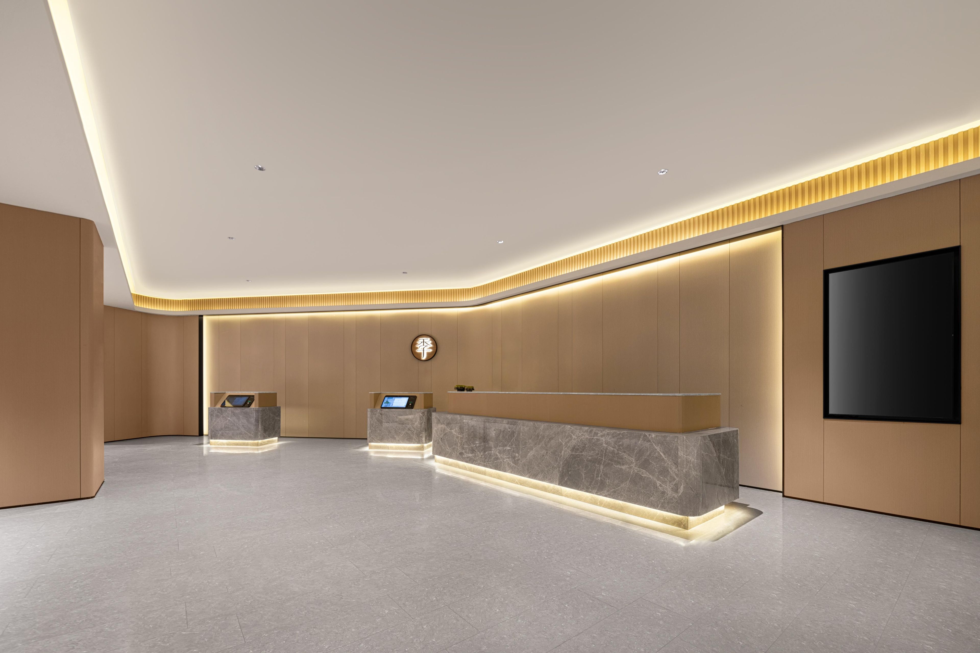 A modern reception area with a marble reception desk, a digital display, and a flat-screen TV mounted on the wall.