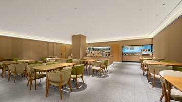 A modern dining area with multiple tables and chairs, a central counter with a display, and a kitchen in the background.