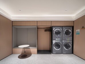 A compact laundry room with a built-in washer and dryer, a small seating area, and a wall-mounted rack. - JI Hotel Xian Bell Tower North Street Metro Stati (Xi'an)