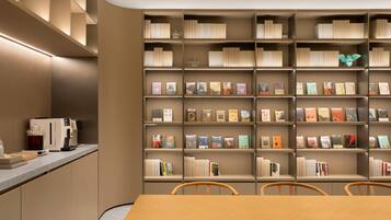 A modern library with bookshelves, a coffee machine, and a wooden table with chairs.