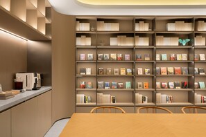 Eine moderne Bibliothek mit Bücherregalen, einer Kaffeemaschine und einem Holztisch mit Stühlen.