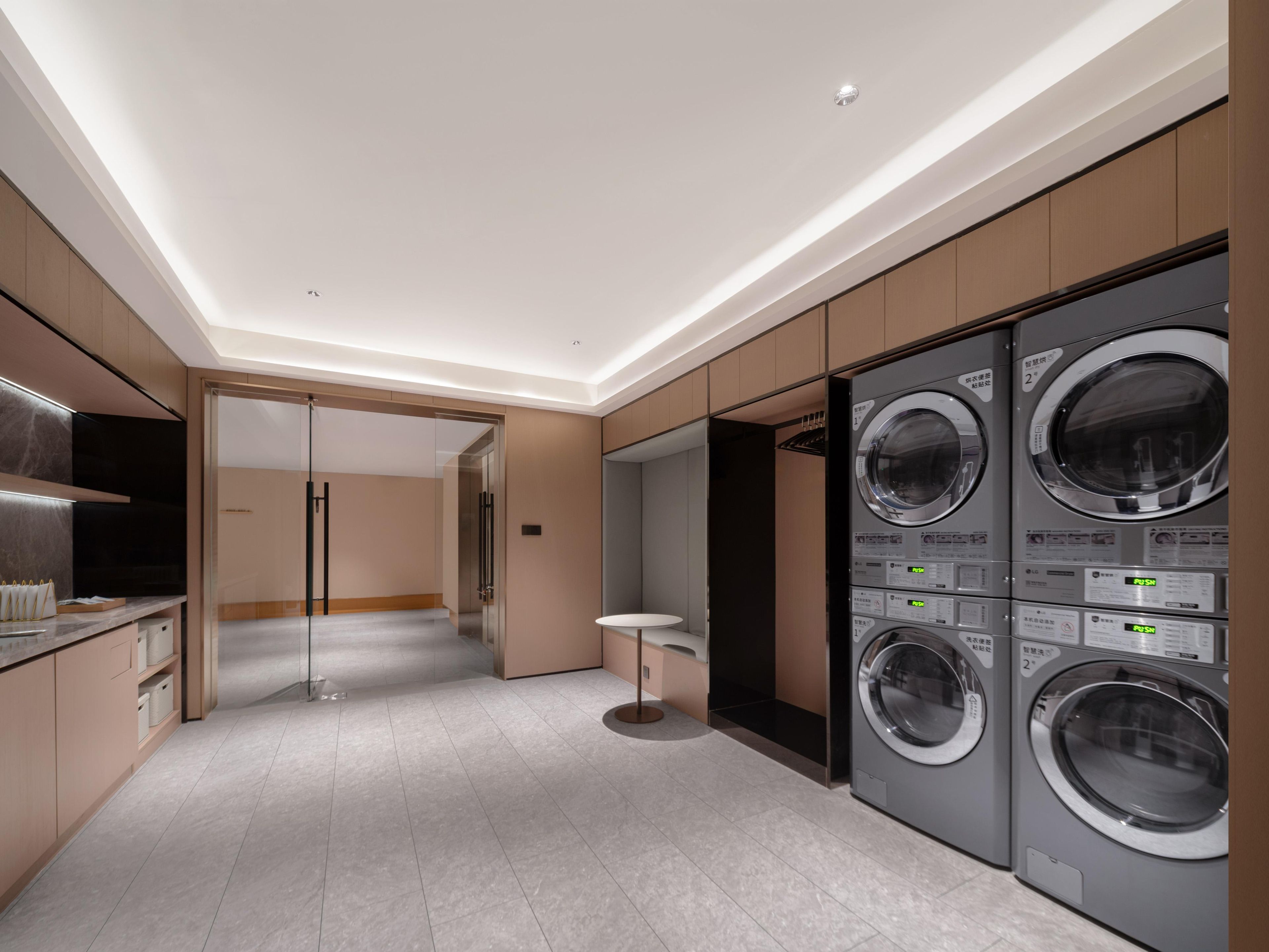 A modern laundry room with built-in washers and dryers, a glass door entrance, and a minimalist design.