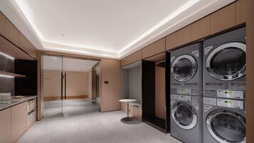 A modern laundry room with built-in washers and dryers, a glass door entrance, and a minimalist design.