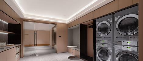 A modern laundry room with built-in washers and dryers, a glass door entrance, and a minimalist design.
