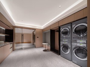 A modern laundry room with built-in washers and dryers, a glass door entrance, and a minimalist design.