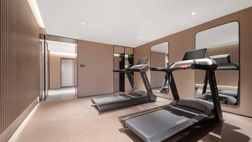 A modern hotel room with a treadmill, a desk with a laptop, and a large mirror.
