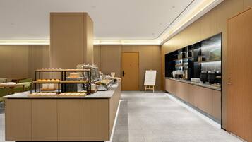 A modern breakfast area with a buffet setup, a coffee station, and a view of the cityscape.