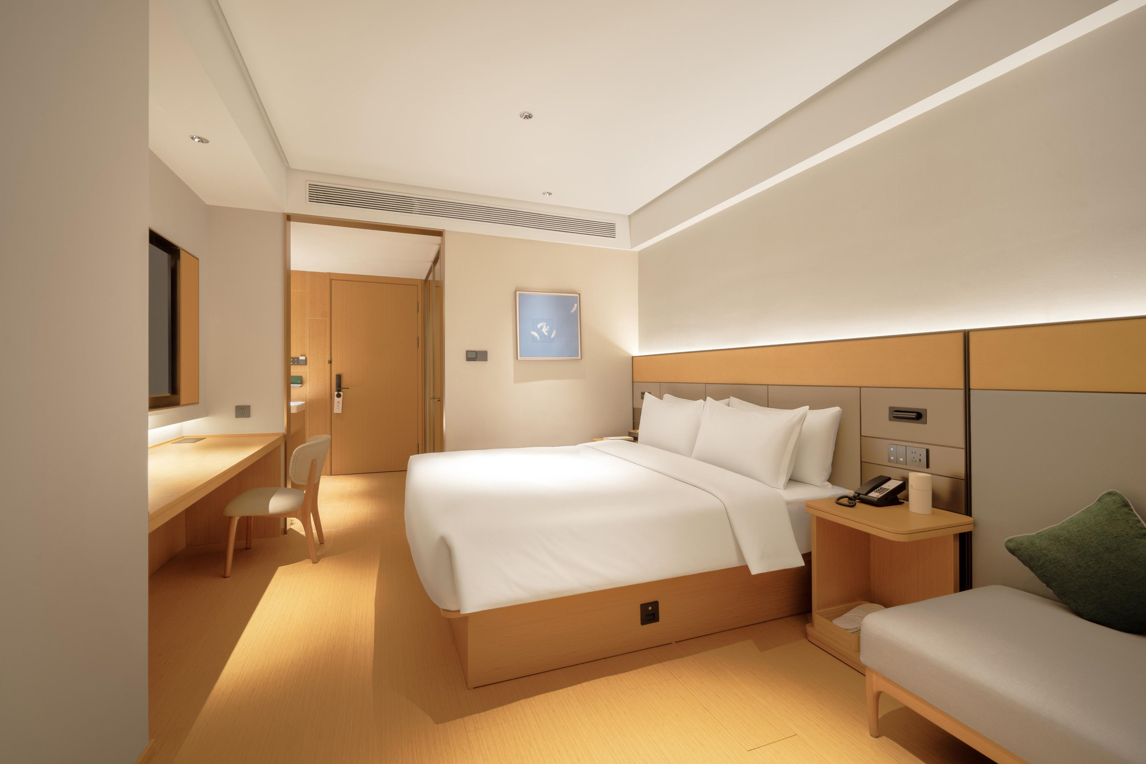 Une chambre d’hôtel comprenant un lit, un bureau, une chaise, une table de chevet avec un téléphone et une petite table de chevet avec une lampe.