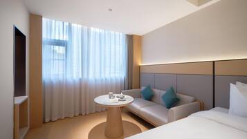 A modern hotel room with a large window, a round table, a sofa, and a bed.