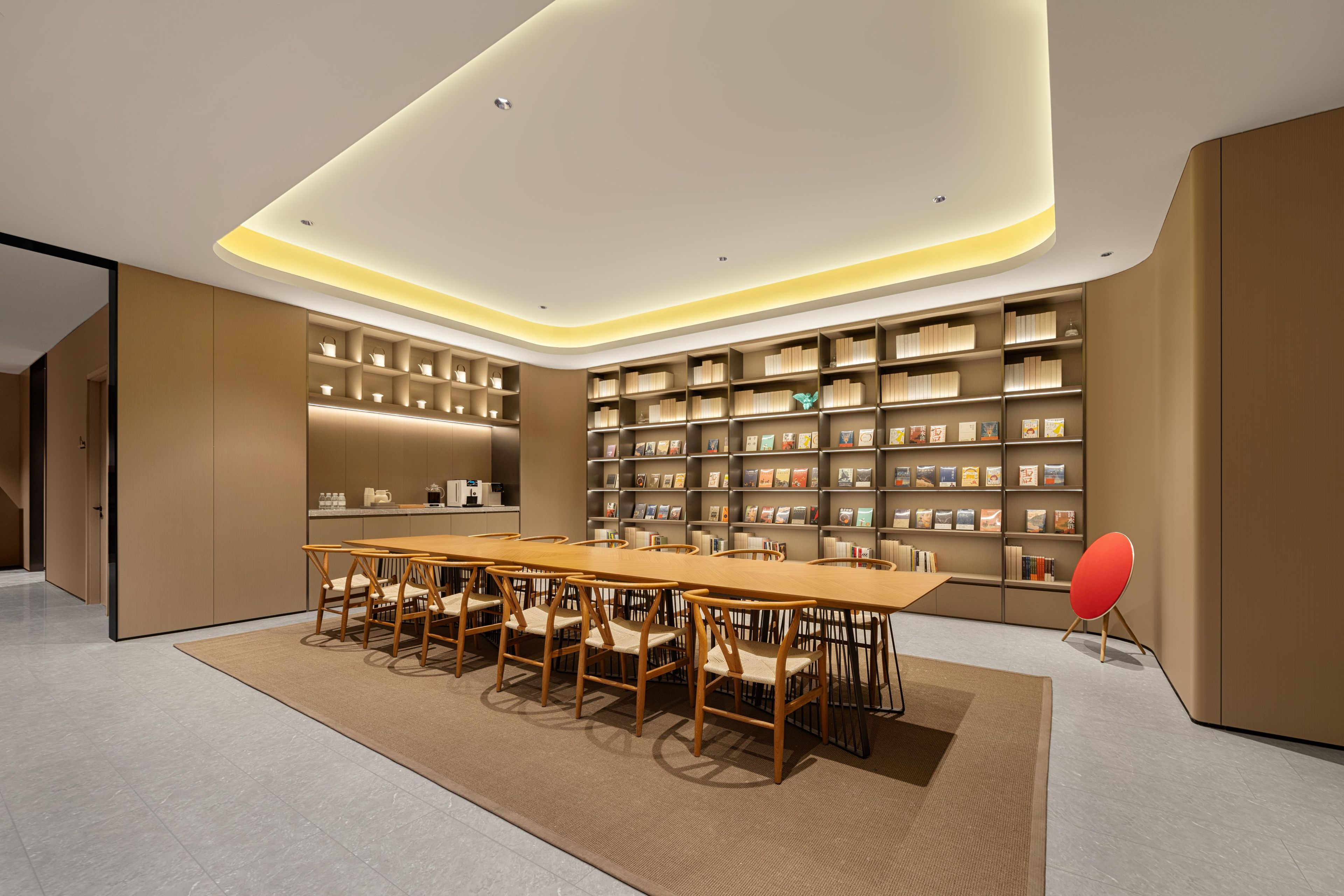 A modern library with a long wooden table and chairs, surrounded by bookshelves.