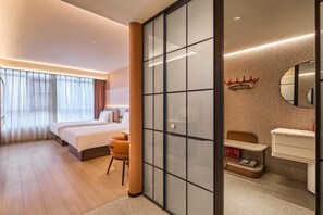 Hotellihuone, jossa on sänky, työpöytä, tuoli, peilillä varustettu kylpyhuone ja liukuovi.
