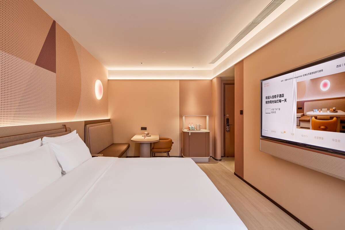 A hotel room with a bed, a desk, a chair, a television, and a wall-mounted screen.