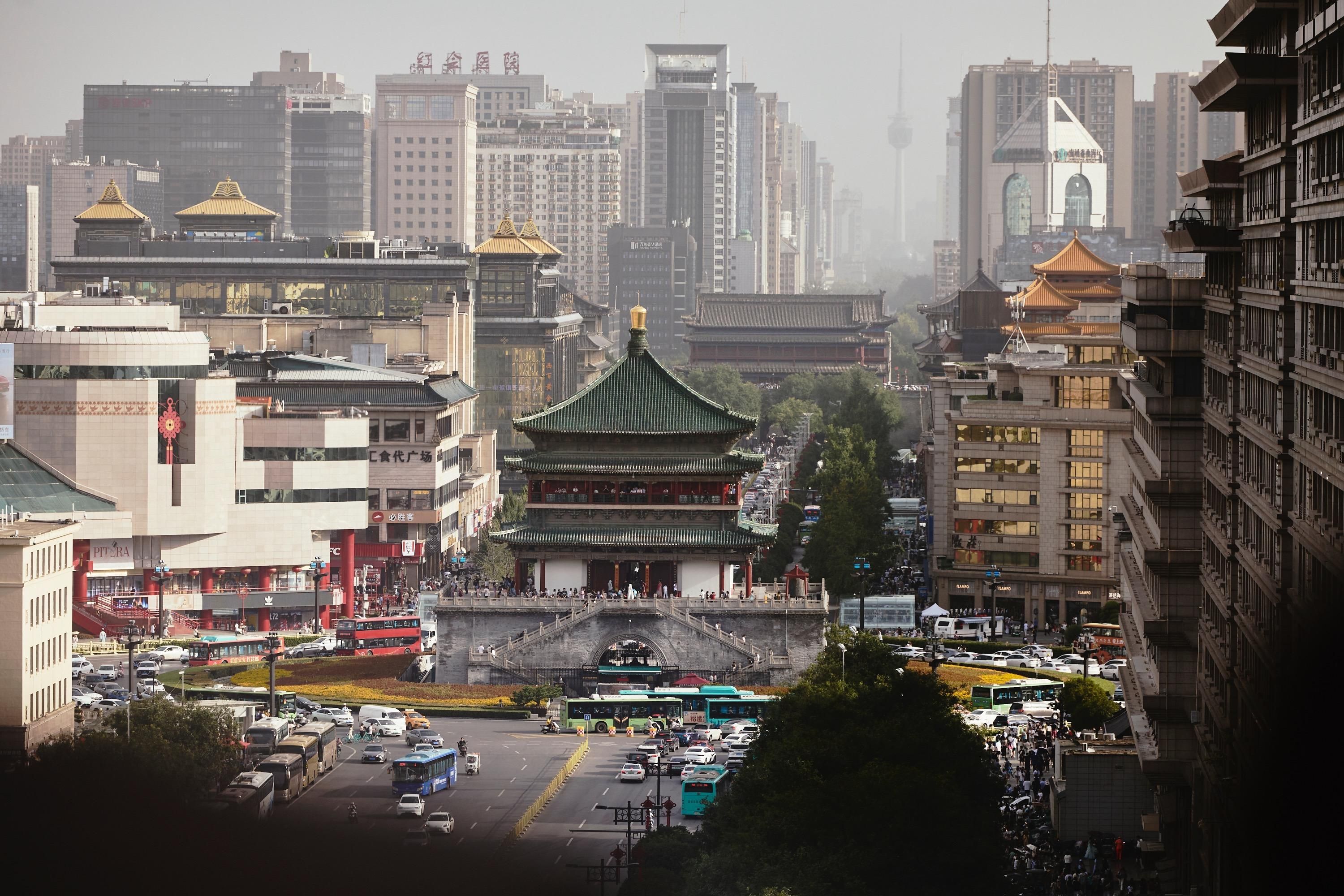 A traditional building with a green roof and golden accents, surrounded by modern high-rise buildings.
